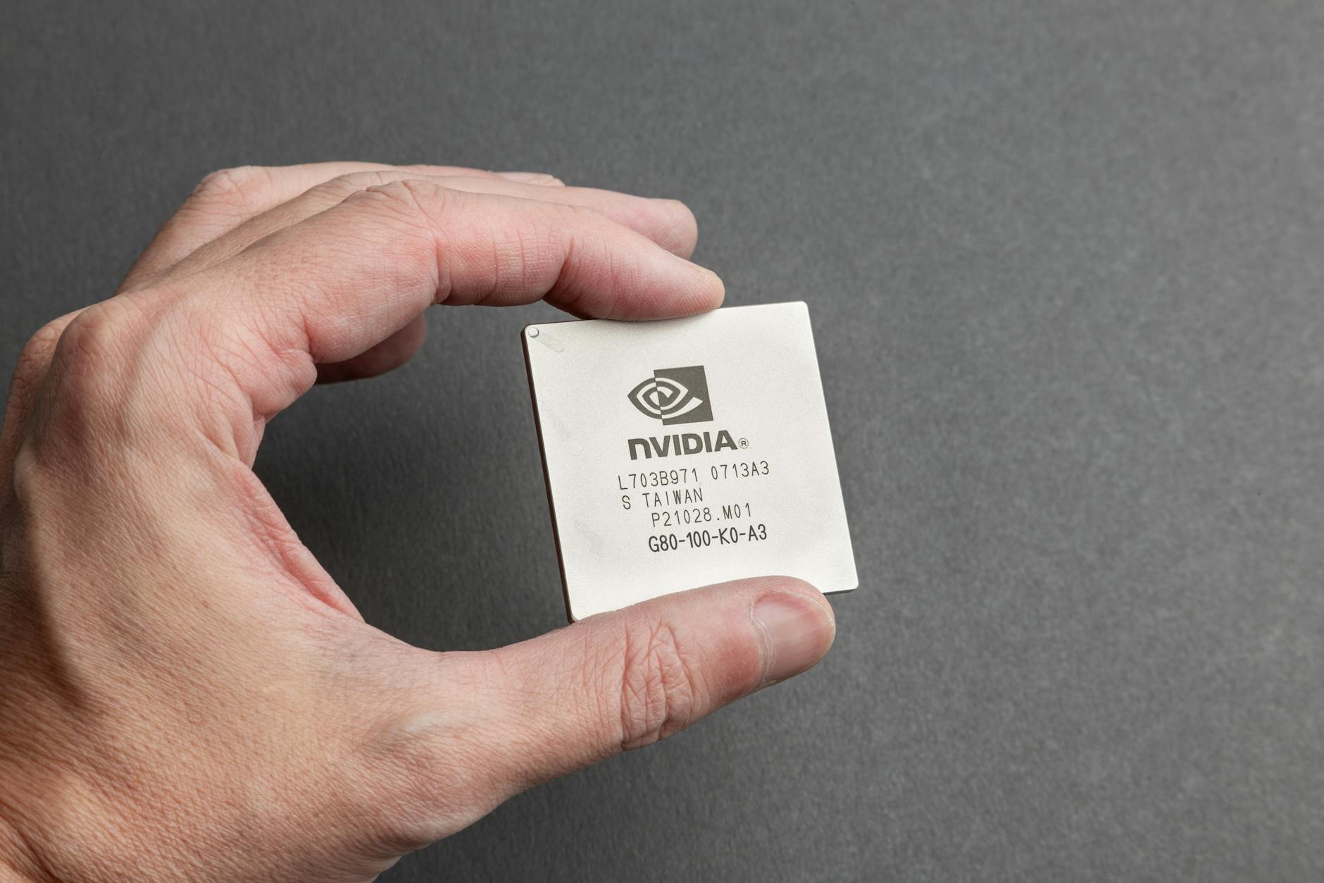 Dłoń trzymająca mikrochip Nvidia na szarym tle