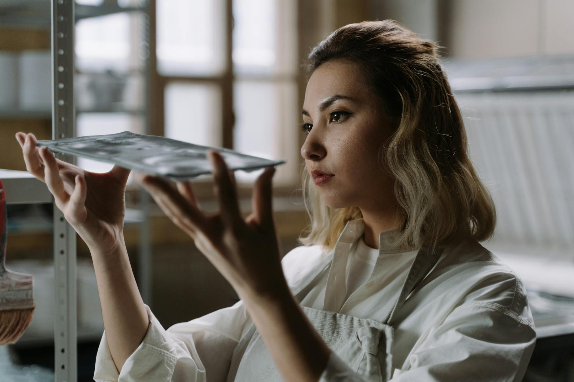 Kobieta w pracowni dokładnie ogląda ręcznie wykonane szklane naczynie