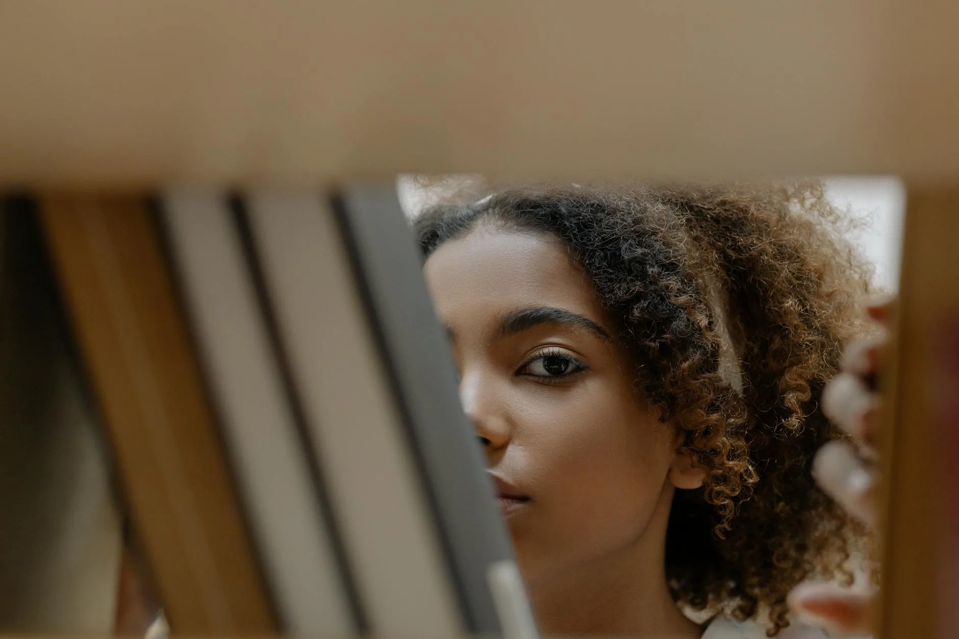 Kobieta zaglądająca między książki na półce, patrząca prosto w obiektyw