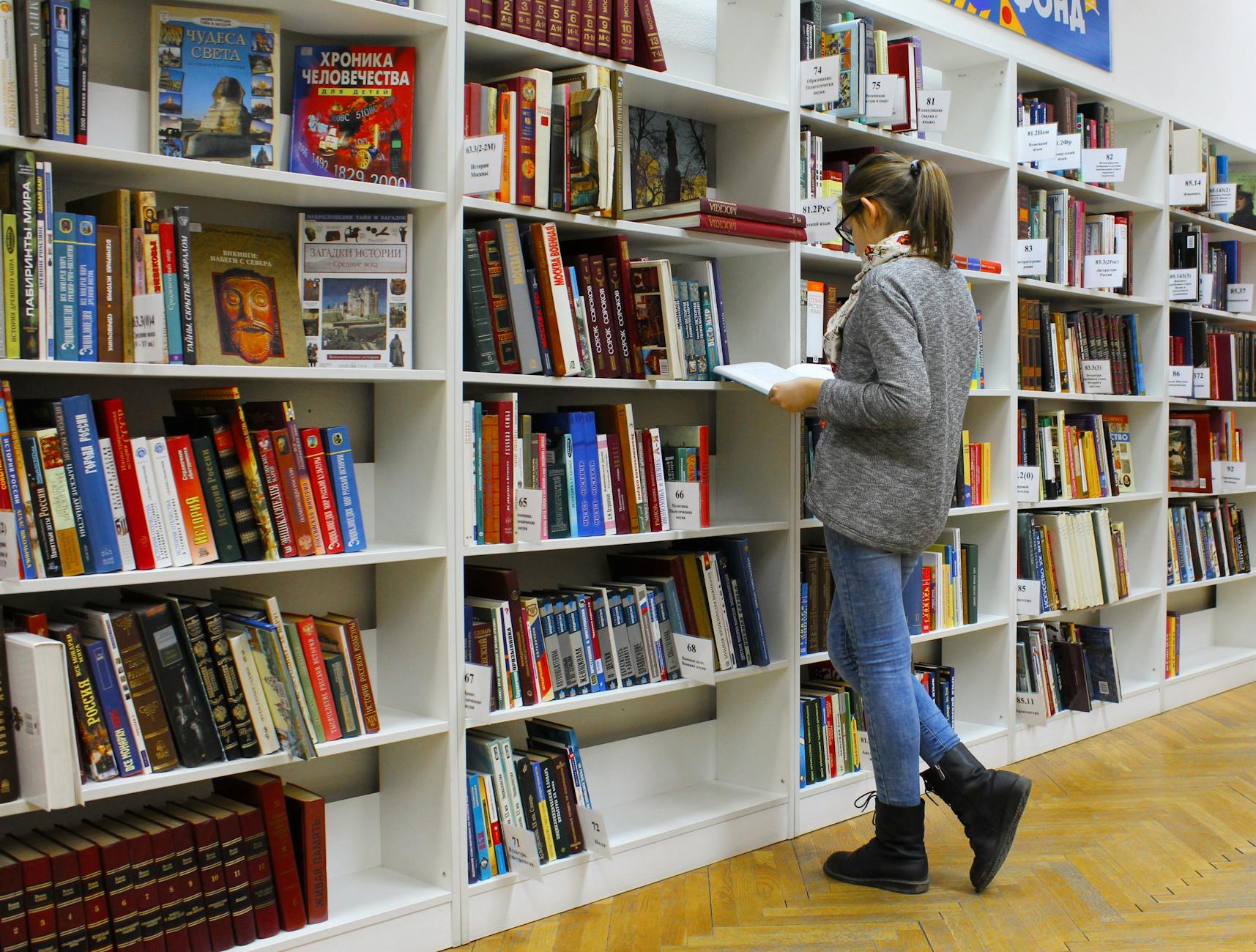 Studentka czyta książkę między regałami w bibliotece