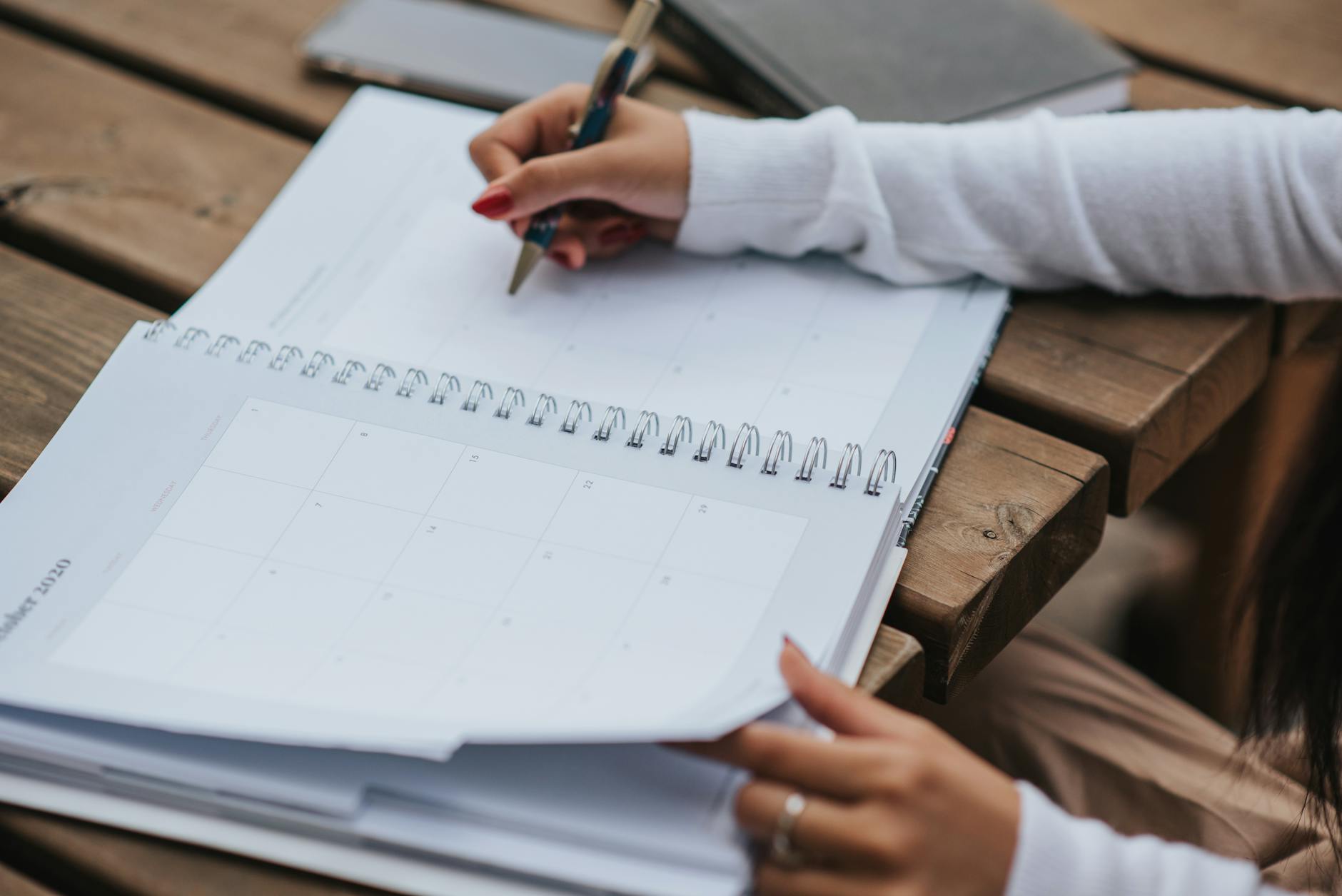 Studentka planuje naukę w plannerze przy drewnianym stole na zewnątrz
