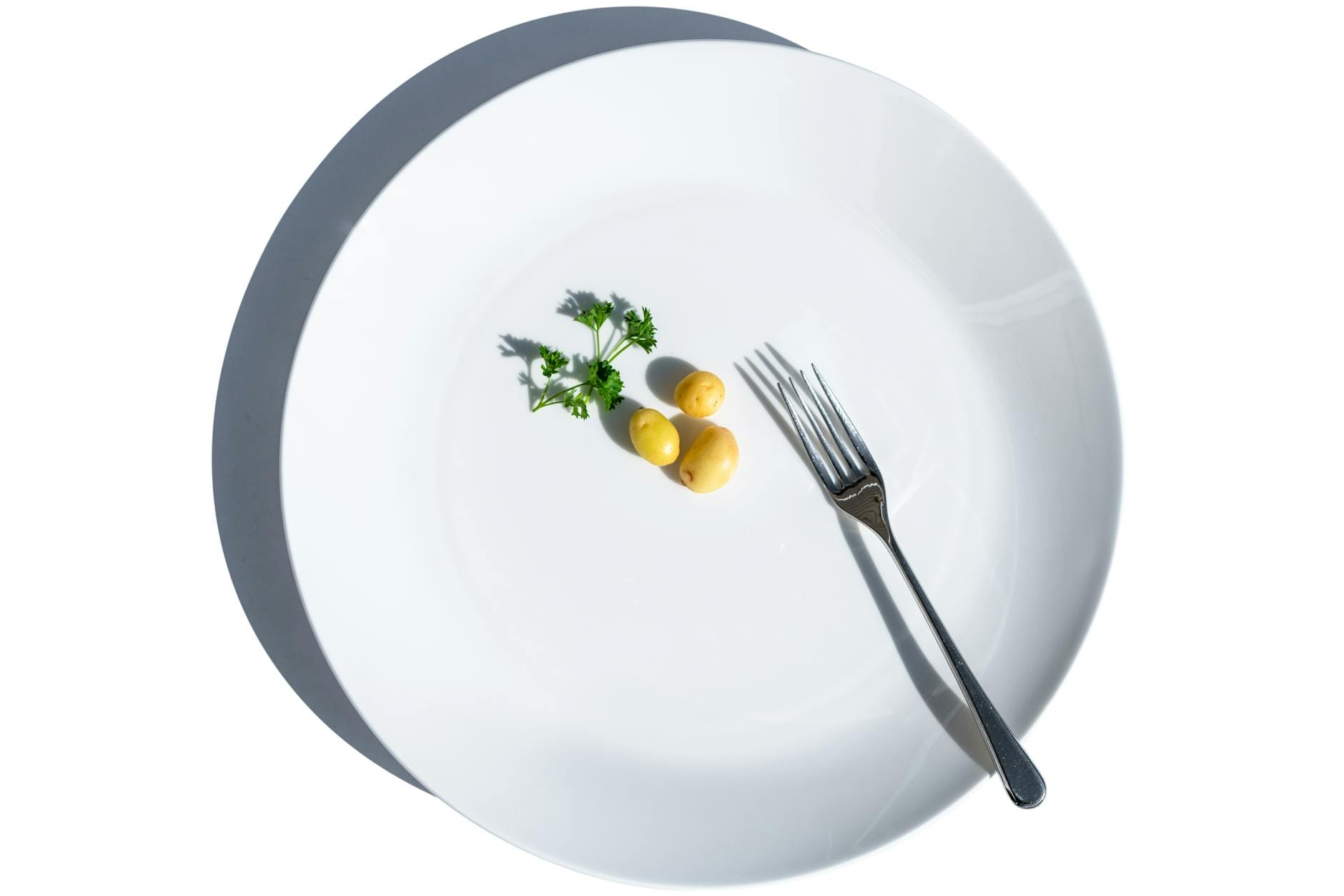 Ziemniaki z natką pietruszki na białym talerzu i widelec, symbol diety