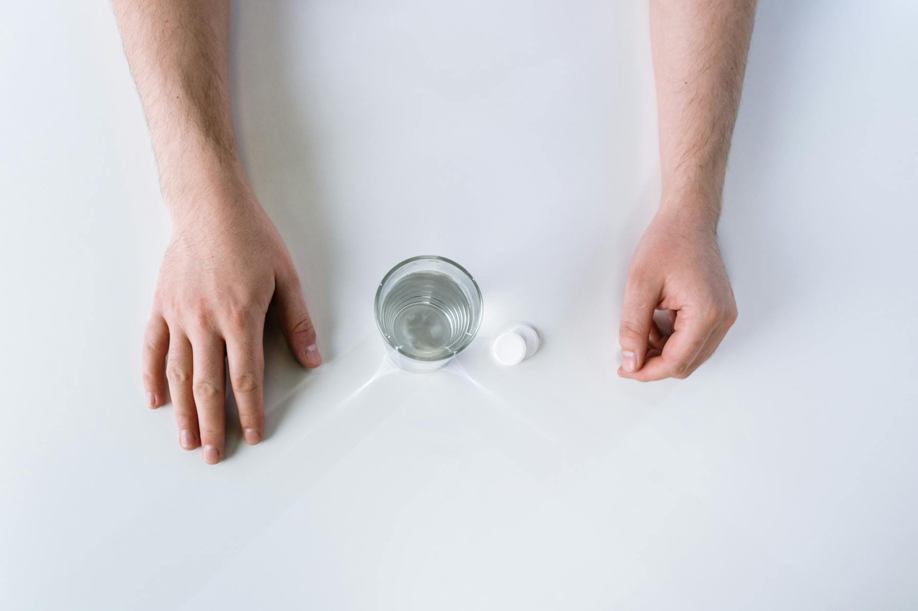 Tabletka musująca przy szklance wody widziana z góry na białym tle