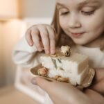 Pierwsze rozstania bez paniki, czyli jak mądrze przygotować dziecko do żłobka i przedszkola Uśmiechnięte dziecko ogląda ręcznie robione mydło z suszonymi kwiatami
