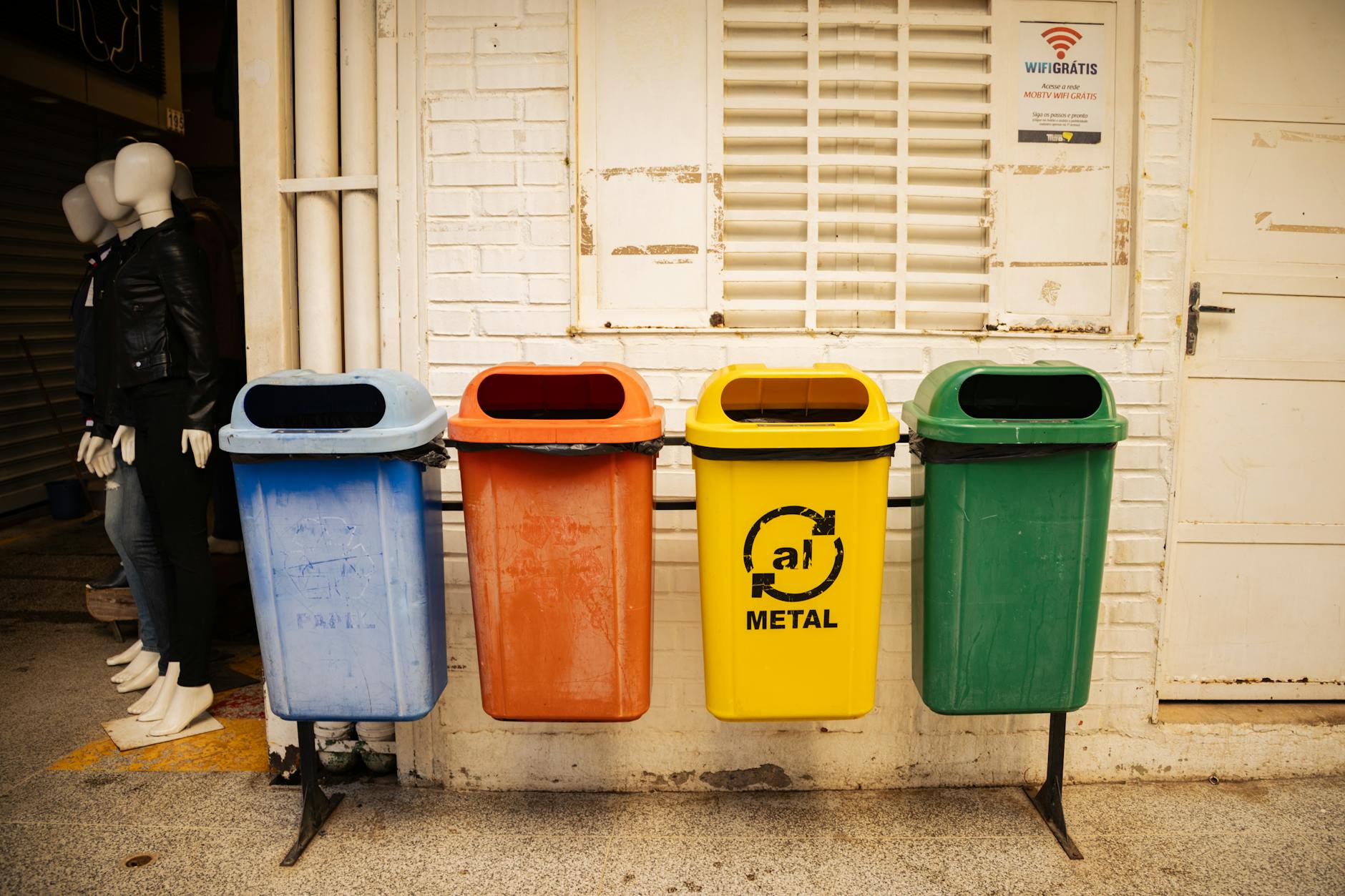 Cztery kolorowe pojemniki do recyklingu stojące przy ceglanej ścianie