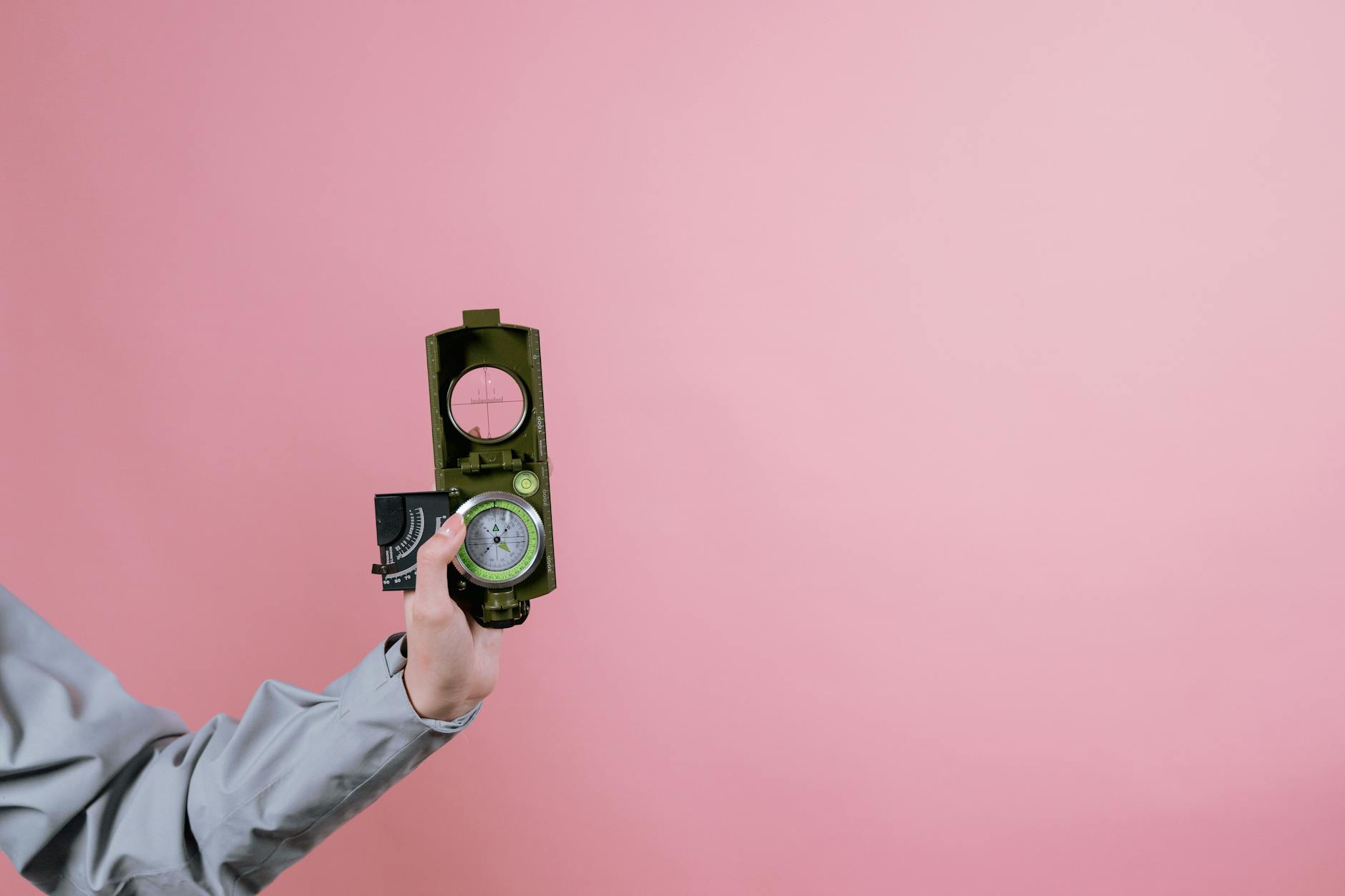Dłoń trzyma wojskowy kompas na różowym tle