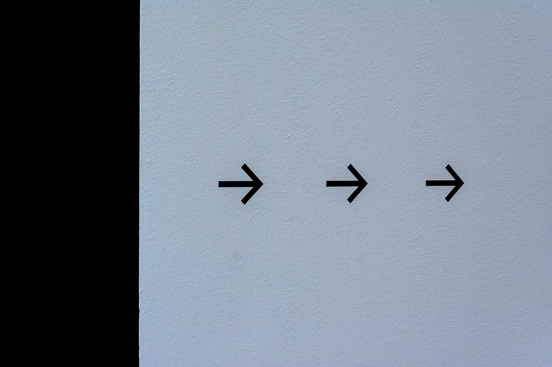 Trzy czarne strzałki w prawo na białej ścianie symbolizujące kierunek czasu