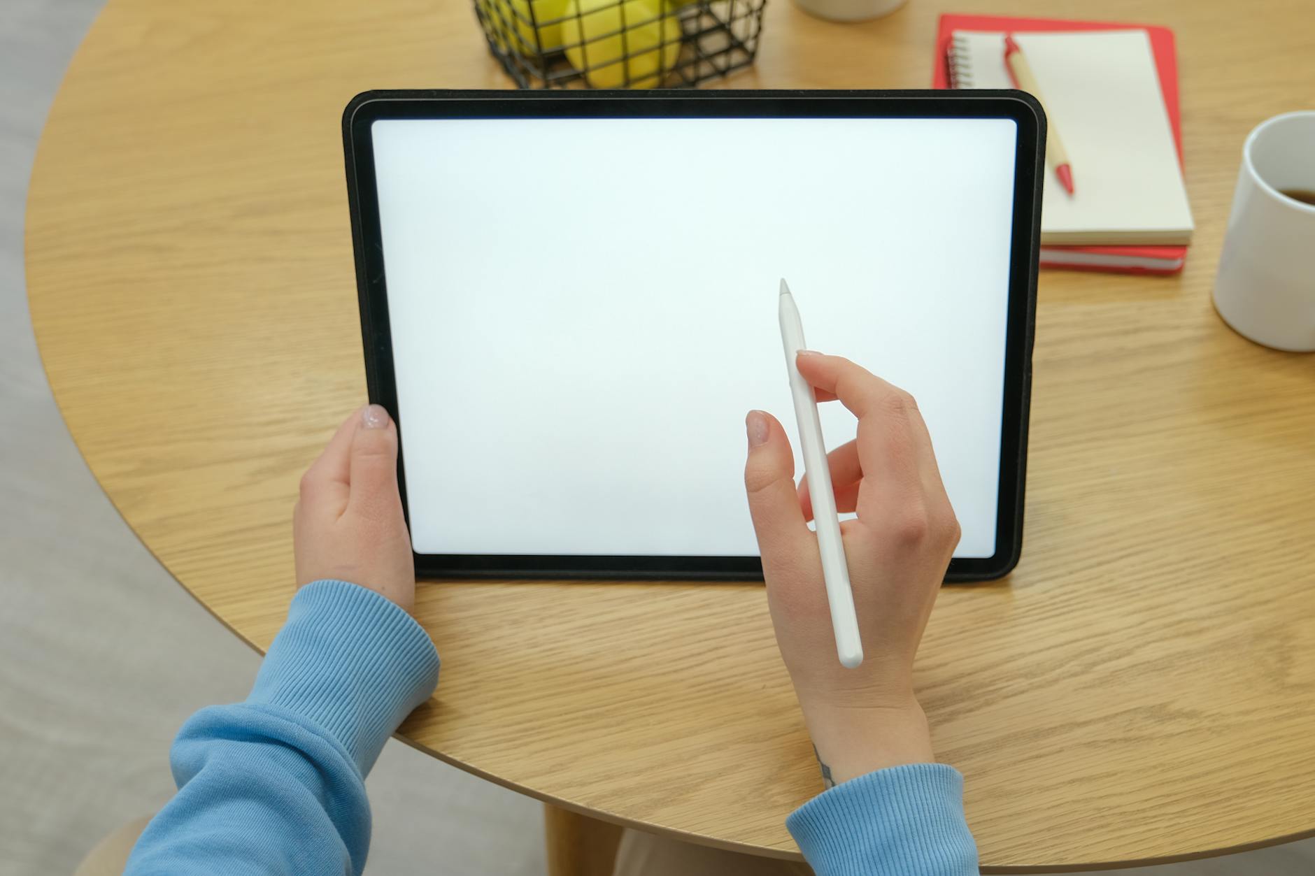 Dłonie trzymające rysik i tablet na drewnianym biurku