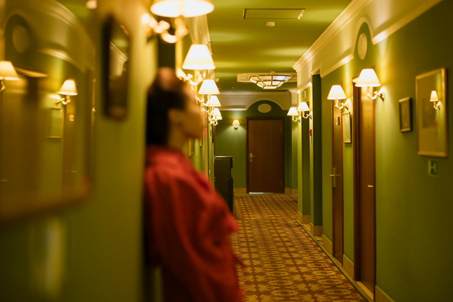 Kobieta w czerwonej sukience oparta o ścianę w ciemnym korytarzu hotelu