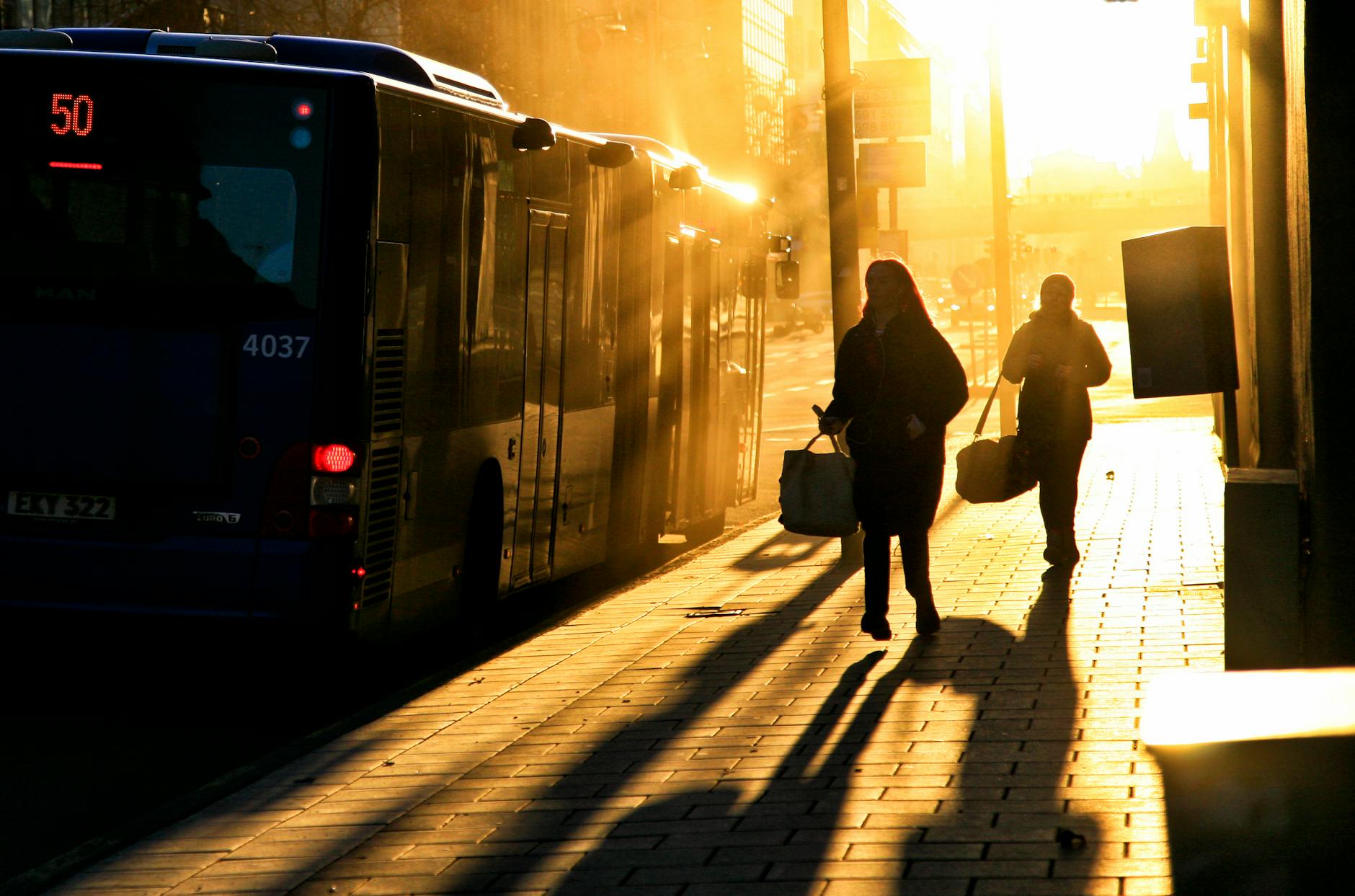 Sylwetki ludzi spieszących do autobusu o wschodzie słońca w Sztokholmie