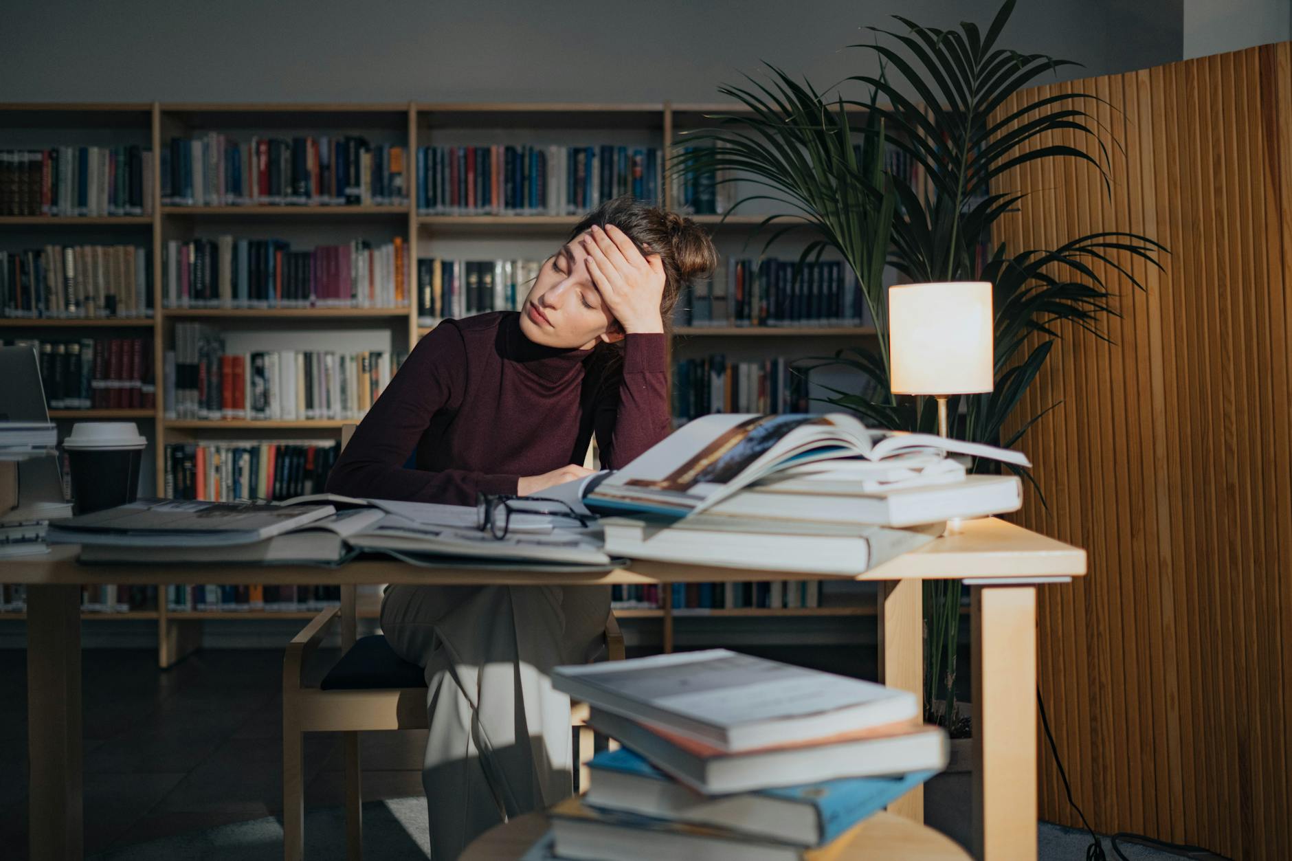 Zmęczona studentka przy biurku w bibliotece, otoczona stosami książek