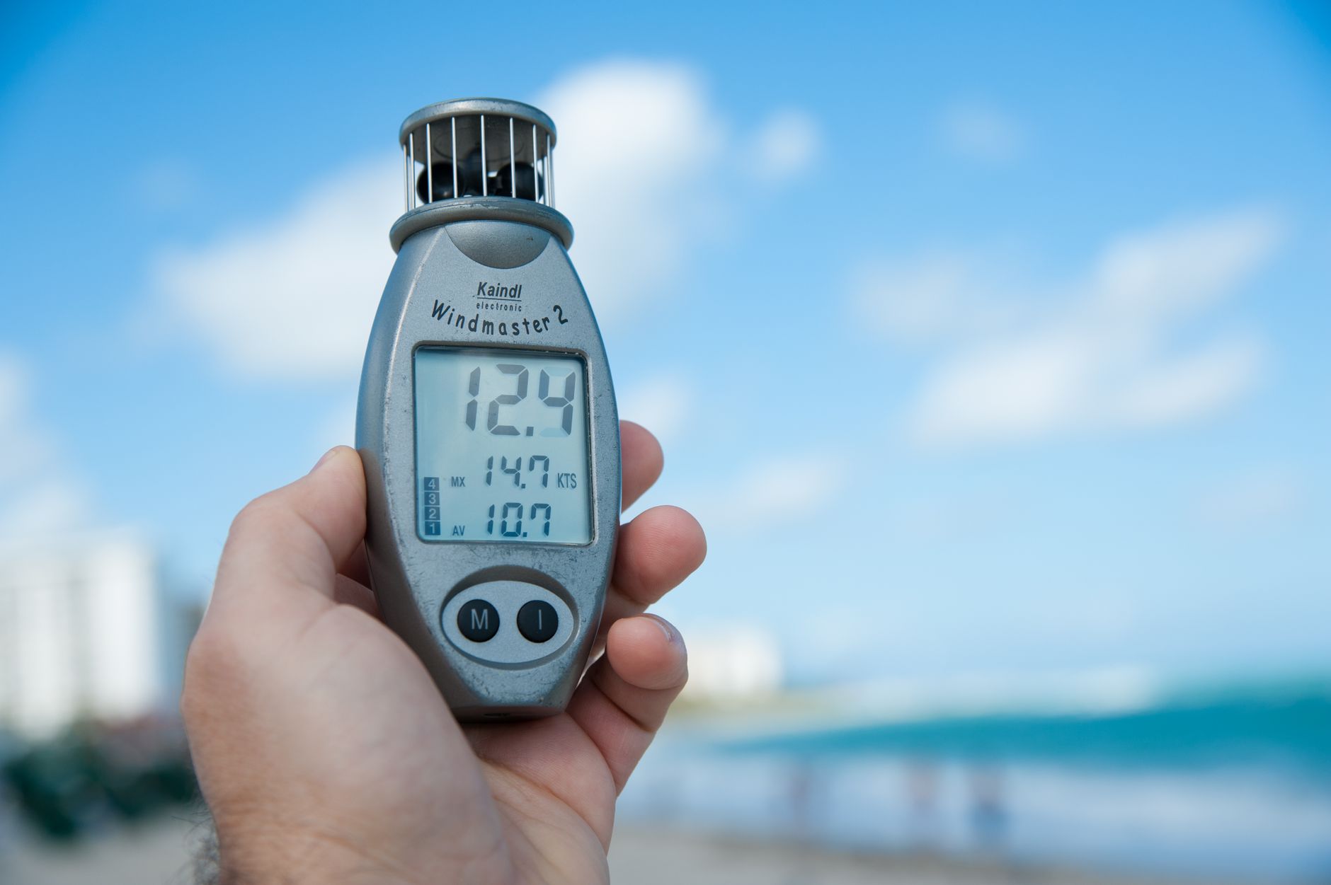 Dłoń trzymająca anemometr na tle błękitnego nieba i plaży